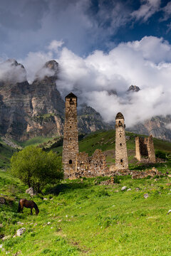 Sunny afternoon in the Caucasus mountains. Nii medieval tower complex consists of combat towers and residential buildings, a few ancient crypts are located on the mountain range nearby.