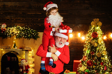 Merry Christmas and Happy Holidays. Santa Claus with child at home. Kid boy and father in Santa costume with Christmas present.