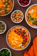 Pumpkin puree soup of butternut squash in bowls with chickpeas and green onions, pumpkin and pomegranate seeds, top view on plates with food on brown background
