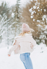 Close up portrait of an beautiful girl in a woolen sweater enjoying winter moments. Outdoors photo of a short-haired lady in a pink hat having fun on a snowy morning on a blurred nature background.