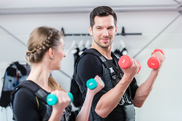 Fitness couple exercising with weights in ems gym looking at each other