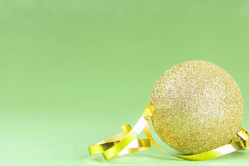 Golden ball with a golden ribbon on a green background. Christmas decorations. New Year. Christmas. Copy space