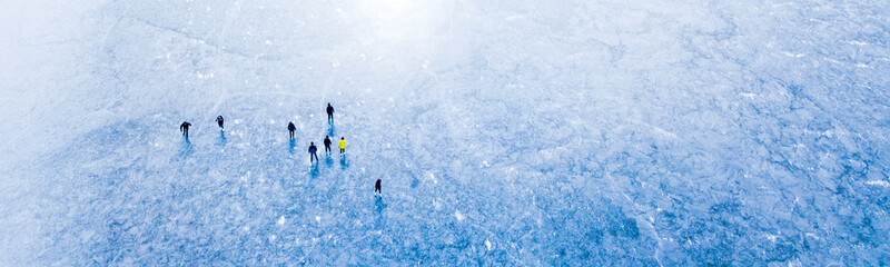 Aerial view of frozen lake with many ice skaters on the ice. Beautiful winter sunny day outdoor. Background concept. - obrazy, fototapety, plakaty