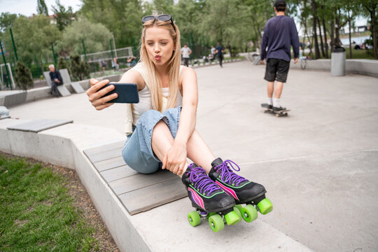 young woman in rollers skates taking selfie on cellphone in skate park.