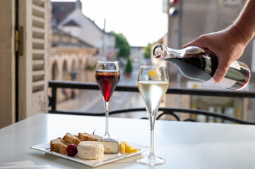 Drinking of Kir Royal,  French aperitif cocktail made  from creme de cassis topped with champagne, typically served in flute glass, with view on old French village