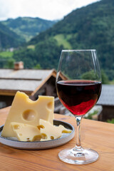 Cheese collection, French cow cheese emmental, glass of red wine from Savoie and french mountains village in Haute-Savoie on background