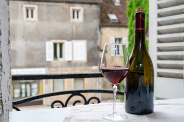 Tasting of burgundy red wine from grand cru pinot noir  vineyards, glass and bottle of wine and view on old town street in Burgundy wine region, France