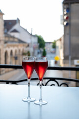 Drinking of Kir Royal,  French aperitif cocktail made  from creme de cassis topped with champagne, typically served in flute glass, with view on old French village
