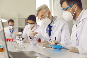 Team of research scientists in protective respiratory face mask and sterile white coat working lab...