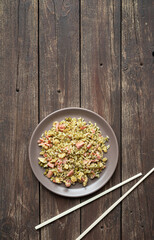 Cantonese rice or Chinese fried rice in a plate and wooden chopsticks on a dark wooden old table, top view with copy space
