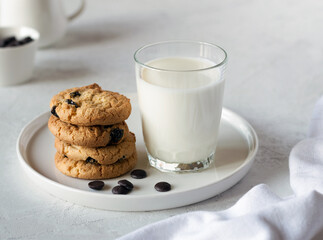 Delicious cookies with chocolate on a white plate and fresh milk in a glass on a light table. An idea for a children's breakfast or snack. Selective focus