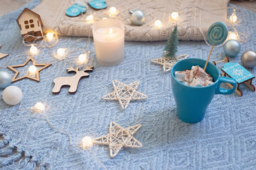 Fototapeta na wymiar Beautiful cozy christmas background with garlands, a candle in a glass, a cup on a knitted blue plaid