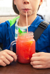 Summer refreshing fruit cocktail with a straw in the hands of a teenager. A child drinks lemonade in a cafe.