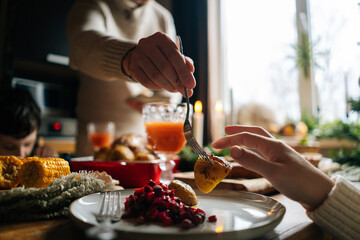 Cropped shot of unrecognizable young man arranging food on plates to wife and son standing at festive Christmas table during holiday family party. Happy people having dinner xmas party and talking.