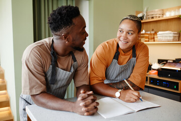 Portrait of young African American man and woman starting workday in modern cafe with creating new...