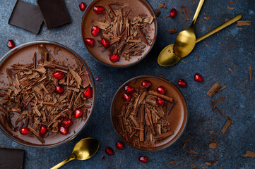 Chocolate panna cotta decorated with chocolate chips and pomegranate seeds on a blue background....