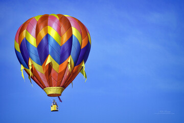 Fototapeta premium A brilliant hot air balloon soars through a clear blue sky.
