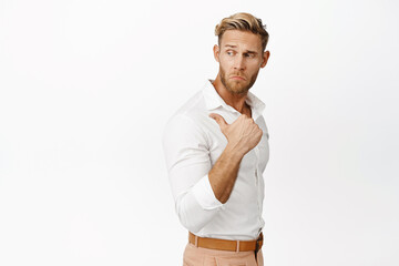 Handsome macho man in white shirt, pointing and looking behind his shoulder, showing sale promo, product on empty copy space, studio background