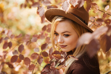Young blonde plus size girl in a hat in the autumn forest in the leaves