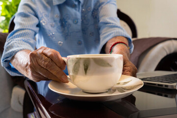 Fototapeta na wymiar Older woman's hands drinking cup of tea with laptop working.