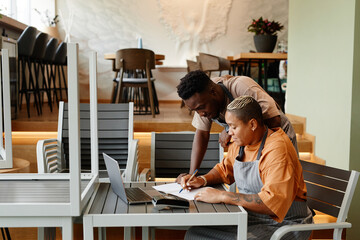Young man and woman working together in modern cafe starting workday checking list of products for...