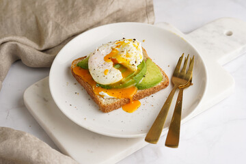 Savoury breakfast - A toast bread with cream cheese, avocado and poached egg on a white plate on marble tray