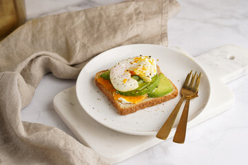 Savoury breakfast - A toast bread with cream cheese, avocado and poached egg on a white plate on marble tray