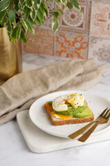 Savoury breakfast - A toast bread with cream cheese, avocado and poached egg on a white plate on marble tray