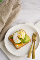 Savoury breakfast - A toast bread with cream cheese, avocado and poached egg on a white plate on marble tray