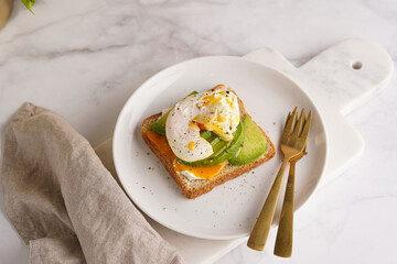 Savoury breakfast - A toast bread with cream cheese, avocado and poached egg on a white plate on marble tray