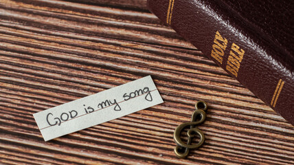 A rustic old treble clef note, handwritten quote: God is my song, and closed Holy Bible on wooden...