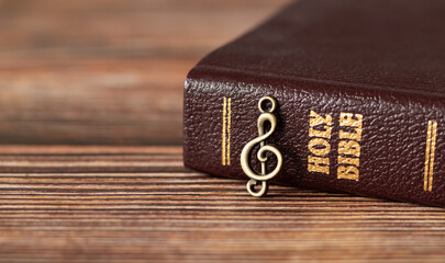 Closed Holy Bible Book with rustic old treble clef note on wooden background. God Jesus Christ is...