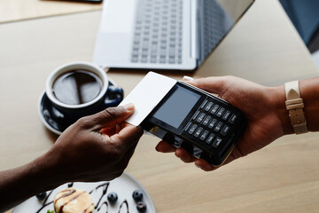High angle close-up shot of unrecognizable man sitting at table in modern cafe paying for order with bank card