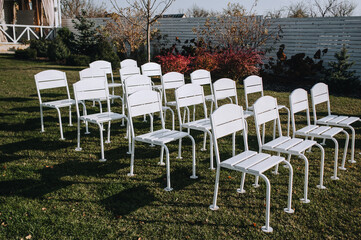 A row of white wooden chairs stands on green grass in a park in nature.