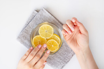 Lemon juice, natural cosmetics. The woman soaking fingernails in lemon juice water - obrazy, fototapety, plakaty