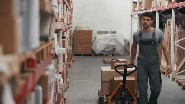 Young male worker in warehouse walks forward with pallet truck