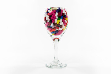 Wine glass filled with pills and capsules on white background.
