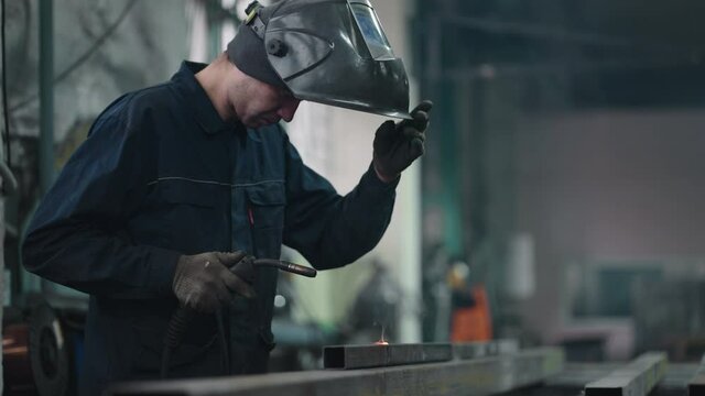 Work in a factory. welder in special mask connects metal parts at bright sparks