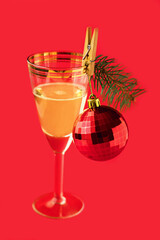 A glass of champagne and a New Year's ball with a spruce twig as attributes of the New Year. Festive attributes on a red background. Festive New Year card.