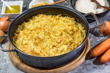 Italian vegan Risotto in a large pan with ingredients - rice, onion, carrots, spices, olive oil
