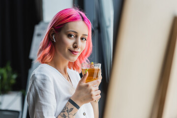 cheerful businesswoman with pink hair and earphone holding cup of tea in office.