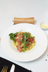 Tasty Italian pasta appetizer with basturma and fresh basil on top on a white table background with docures