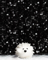 Christmas decorations view of white artificial hedgehog on dark background with silver colors bokeh and artificial snow. Holidays concept with copy space at the top