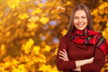 Beautiful young woman relaxing at park during autumn season with foliage in the background.