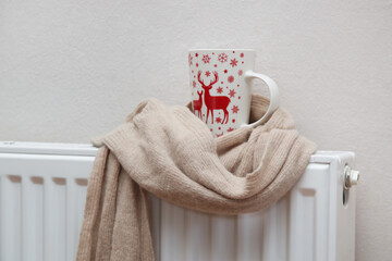 Photo of tea mug wrapped in woolen scarf on radiator. Heating season concept. 