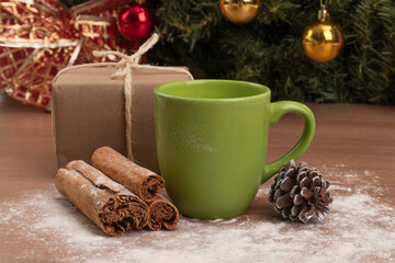 green cup next to a gift box, cinnamon and sugar decorating, background with a christmas tree, holiday celebration in december, objects in studio
