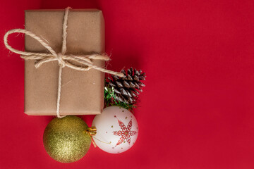 pink background with a gift box wrapped in paper with a cord bow next to Christmas balls to decorate, objects in studio, holiday
