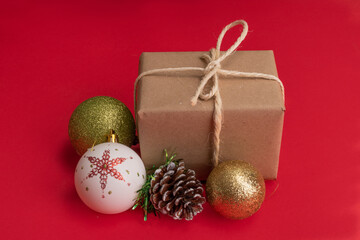 pink wallpaper with a gift box wrapped in paper with a cord bow next to Christmas balls to decorate, objects in studio, holiday concept