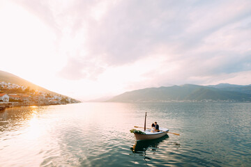 Man rolls woman in a boat with flowers on the water on the mountains and sunset