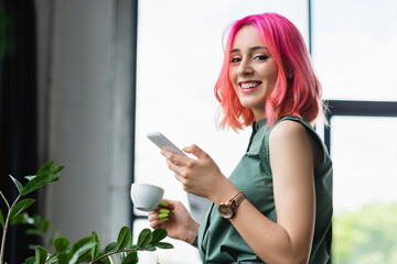 cheerful businesswoman with pink hair and piercing holding cup of coffee and smartphone. - Powered by Adobe